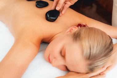 Lüks tatil köyündeki kaplıcalarda sıcak taş masajı. Gün ışığı sükunet ortamında, mutlu kadın müşteri bazalt taş masajından zevk alıyor. Rahatlatıcı bir sıcaklıkla vücudun üzerinde süzülüyor. Sessiz.