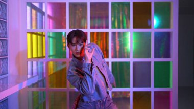 Gece kulübünde kameraya bakarken güneş gözlüklü Asyalı sanatçının serbest dans edişini yakından çek. Mutlu sokak dansçısı dans ediyor ve renkli parlak neon ışıklı ayak izlerini gösteriyor. Mutluluk.