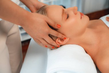 Yakın plan kadın stres önleyici kafa masajı yapmaktan ve lüks tatil beldesi veya otel spa salonundaki modern ışık ortamında yüz güzelliği eğlencelerini şımartmaktan zevk alıyor. Sessiz.