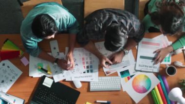 Tasarımcı fikirleri yazarken proje yöneticisinin yukarıdan aşağıya bakan görüntüsü. Akıllı iş adamları logo tasarımı fikrini açıklarken tasarımcılar palete bakarken temayı seçiyorlar. Sempozyum.