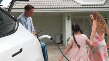 Mutlu küçük kız, ailesinin EV şarj istasyonundan elektrikli aracını şarj etmesine yardım ederken çevre dostu ve enerji sürdürülebilirliğini öğreniyor. EV araba ve modern aile kavramı. Titiz