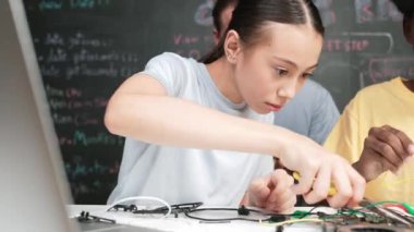 Çeşitli öğrenciler elektronik alet tamir tahtasını kullanırken, beyaz öğretmenler de STEM teknoloji sınıfında robot araba hazırlamaya yardım ediyor. Kablo ve anakart kullanarak çalışan çok kültürlü insanlar. Öğretim