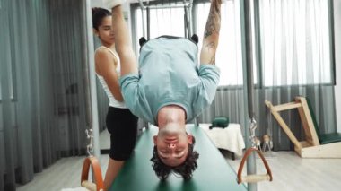 Eğitmen rehberliğinde Pilates Cadillac 'ta ters bacak yükseltme pratiği yapan sağlıklı bir müşteri. Çekirdek dayanıklılığını ve üst vücut dengesini arttırmak için Cadillac 'ı geren adam. Alışkanlık.