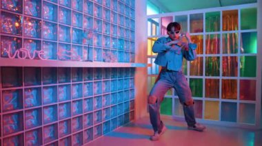 Gece kulübünde kameraya bakarken güneş gözlüklü Asyalı dansçı serbest dans ediyor. Mutlu sokak dansçısı dans ediyor ve renkli parlak neon ışığı ya da yol gösteren ışıkla ayak seslerini gösteriyor. Mutluluk.