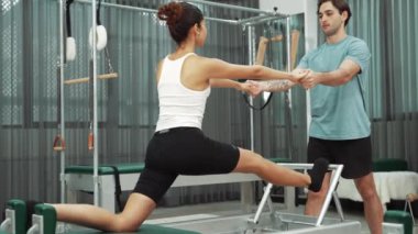 Esneklik ve çekirdek eğitimi için pilates kursunda trapez masasında destek alan bir kadın. Öğrenci dengeyi geliştirmek için reformcuları iki büklüm ediyor. Alışkanlık.