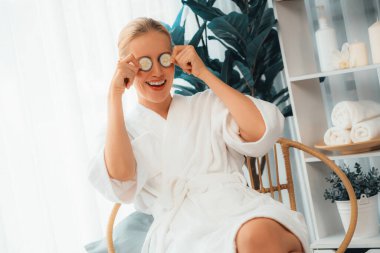 Elinde taze salatalık dilimleri tutan ve bornoz giyen bir kadın tatil köyünde ya da otelde lüks yüz derisi kaplıcalarının tadını çıkarıyor. Yüz ve güzellik tedavisi için cilt bakımı. Sessiz.