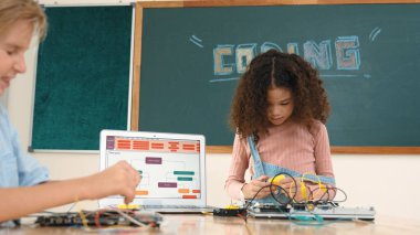 Kız tornavida kullanarak elektronik tahtayı tamir ederken ayakta duruyor. Amerikalı öğrenci ve beyaz çocuk elektrik sistemini denetlemek için birlikte çalışıyorlar. Gemide çalışan meraklı çocuklar. Pedagoji.