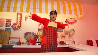 Profesyonel Asyalı restoran işçisi dans ediyor ve yemek barının arkasında duruyor. Kırmızı tişörtlü ve kırmızı önlüklü çekici garson kameraya bakarken serbest stil müziğe yöneliyor. Çılgın dans. Mutluluk.