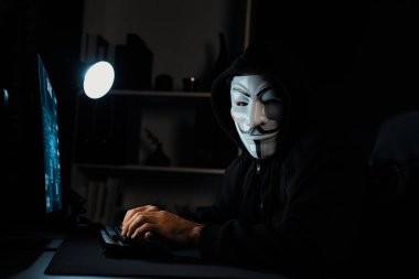 Kameraya bakan beyaz sırıtan isimsiz suçlu maskesi ana veritabanı sunucu sistemi aracılığıyla bilgisayar fidye şirketinin gizliliğinde başarıyla hacklenen virüs şifrelemesi yüklüyor. Tahmin et..