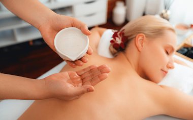 Masör elleri kadının sırtına aroma yağı döküyor. Masözler lüks otellerdeki kaplıca salonundaki müşteriler için yağ masajı prosedürü hazırlıyorlar. Aroma yağı vücut masajı konsepti. Sessiz.
