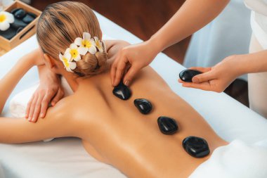 Lüks tatil köyündeki kaplıcalarda sıcak taş masajı. Gün ışığı sükunet ortamında, mutlu kadın müşteri bazalt taş masajından zevk alıyor. Rahatlatıcı bir sıcaklıkla vücudun üzerinde süzülüyor. Sessiz.