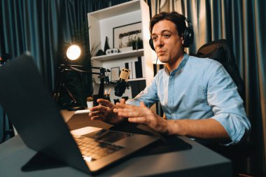 Sunucu kanalı akıllı yayıncı laptopta canlı sosyal medya uygulaması arıyor, kulaklık takıyor ve modern ofis stüdyosundaki mikrofonu kullanıyor. Bireysel.