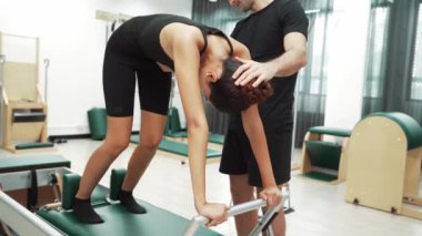 Kadın antrenör desteğiyle reformcuya ileri derecede pilates yapıyor. Çekici bir öğrenci pilates yaparken beden eğitiminin çekirdeğini güçlendirmek için fil pozu veriyor. Alışkanlık.