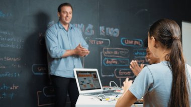 Kafkas öğretmeni alkışlayarak öğrencileri kodlamayı veya programlamayı teşvik etmek için alkışlıyor. Çeşitli öğrenciler STEM sınıfına katılırken başarılı bir projeyi kutlamak için el çırpıyorlar. Öğretim.