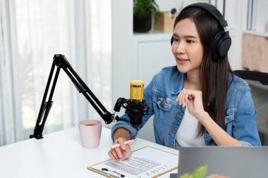 Sosyal medyada kulaklıkla canlı yayın yapan Asyalı sunucu modern stüdyoda yaşam koçluğu veya pazarlama dinleyicilerini selamlıyor. Taktik.