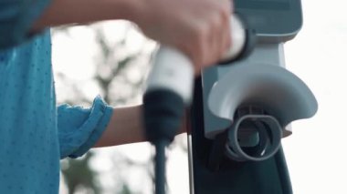 Kapalı alan kadını, doğal yeşil parktaki otoparkta EV elektrikli araba aküsünü şarj ediyor. Sürdürülebilir ve çevre dostu seyahat için şarj edilebilir araç için temiz enerji teknolojisi. Titiz
