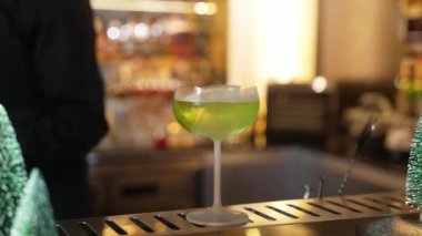 Kesilmiş barmen karamelize edilmiş narenciye dilimini yeşil Midori ekşi kokteyli ile küp buzlu dilimleyip şık saplı bardakta servis ediyor. Sofistike bar ayarları için mükemmel bir Noel ağacı teması. Vinosity.