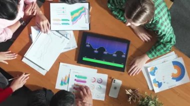 İş adamının tablet ekranını kullanmasına ilişkin en iyi bakış açısı artan grafiği kullanırken, farklı pazarlamacılar da fikir paylaşımı veya planlama stratejisini borsa istatistikleri etrafa saçılmış bir şekilde toplantı masasında paylaşıyorlar. Cemaat.