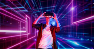 VR gözlüklü profesyonel erkek oyuncu parlayan neon ışıkla oyun oynuyor. Heyecanlı oyuncu artırılmış gerçeklik teknolojisi yeniliklerini kullanarak metaevrene bağlanmayı seviyor. Yaratıcılık.