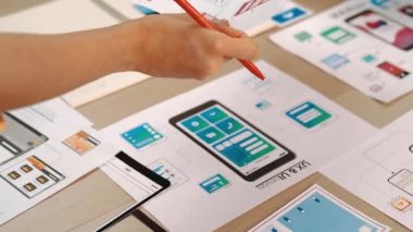 Girişimci şirket çalışanının el odaklı hali ofis çalışma alanındaki akıllı yöneticiye mobil uygulama için kullanıcı arayüzü prototipi sunar. UX UI tasarımcısı kağıt üzerinde simge tasarımının işlevini açıklıyor. Sinerjik