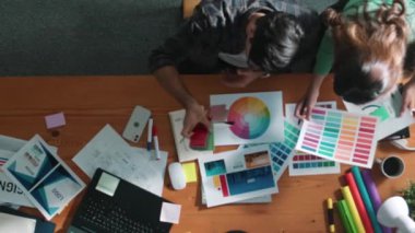 Akıllı tasarımcının renkli paletlerden renk seçmesine yardım ederken yukarıdan aşağı görünümü. Dizüstü bilgisayardan logoya bakarken birlikte çalışan ve planlayan iş adamlarının hava görüntüsü. Sempozyum.