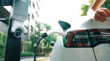 Yavaş çekim çift yazın yeşil sürdürülebilir şehir açık bahçesinde elektrikli araba şarj ile seyahat elektrikli aracın temiz yeniden şarj edilebilir enerjisi için kentsel sürdürülebilirlik yaşam tarzı olarak