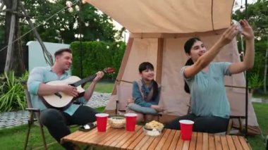 Baba gitar çalarken anne ve kızı bahçede kamp yapıyor. Ebeveynler, genç nesil çapraz kuşak farklılıklarıyla zaman geçirmek için açık hava kamp aktivitelerini kullanıyorlar. Uyumsuzluk.