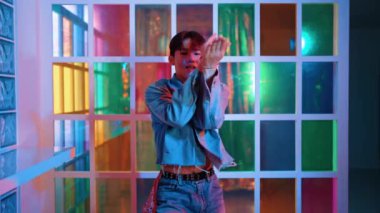 Kameraya bakarken kollarını esneten seksi kıyafetli Asyalı dansçı. Profesyonel sanatçı gece kulübünde renkli neon ışıkları canlı bir şekilde dururken serbest stil dansı yapıyor. Mutluluk.