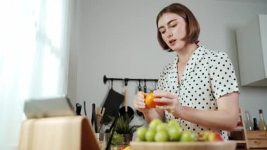 Kafkasyalı anne, modern mutfakta dizüstü bilgisayarda yemek tarifine bakarken salata yapmak için yemek hazırlıyor. Yetenekli ev bekçisi taze sebze kullanarak kahvaltı hazırlıyor. Pedagoji.