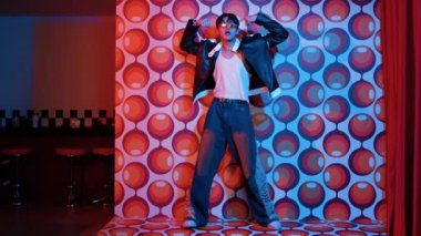 Asyalı break dansçı serbest stile geçiyor ve balon arka planlı kameraya bakıyor. Profesyonel hippi gündelik kıyafet giyer ve gözlük takar. Mutluluk.