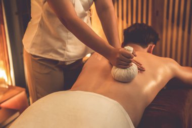 Sıcak bitkisel top spa masaj vücut tedavisi, masör erkek vücuduna nazikçe şifalı bitki torbası bastırıyor. Aromaterapi tesisinin sakinliği ve dinginliği kaplıca salonundaki mumların sıcacık ışığında. Sessiz.