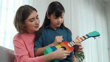 Kafkasyalı bir anne evde akustik müzik öğretirken ukulele çalan mutlu kız. Sevimli çocuk enstrüman öğreniyor. Kafkasyalı mutlu anne ve kız birlikte vakit geçiriyorlar. Pedagoji.