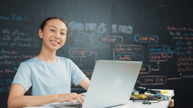 Kara tahtada dizüstü bilgisayar kullanarak akıllı kız programlama sistemi. Lise öğrencisi mühendislik kodları yazıyor ya da STEM teknoloji sınıfında kameraya bakarken bir şey söylüyor. Yaratıcı eğitim. Öğretim.