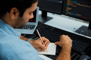 Akıllı IT geliştiricisi laptop ve iki pc ekranda kodlanan kağıtlar üzerine veri notları yazarak modern ofiste uygulama programı güncelleme sürüm sistemi yaratıyor. Tahmin et..