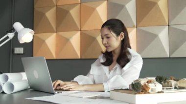 Modern ofiste proje planı, dizüstü bilgisayarı ve mimari modeli olan dizüstü bilgisayar analiz binası yapısını kullanan akıllı bir iç mimar. Asyalı proje yöneticisi bina tasarımını ölçüyor. Yönlendirici.