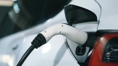 Yavaş çekim yakın EV elektrikli araba şarj istasyonunda fişe takılı, şehir merkezindeki alışveriş merkezinin otoparkında şarj bataryasını şarj ediyor. Elektrikli araç iç organları için temiz yeşil sürdürülebilir enerjisi var.