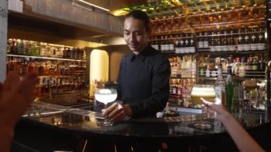 Asyalı barmen karışık kremalı votka bardağı servis ediyor. Güzel bir müşteride buz sunumunda yanmış pembe çiçekli bluz ekliyor. Lüks tezgahta alkol gecesine odaklanıyor. Vinosity.