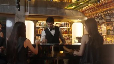 Akıllı barmen, canlı bir gece partisi atmosferinde cin köpüklü cam içeceklerle mükemmel hizmet veriyor. Güzel bir müşteri ve arkadaşı arkadaki tezgahta oturuyor. Vinosity.