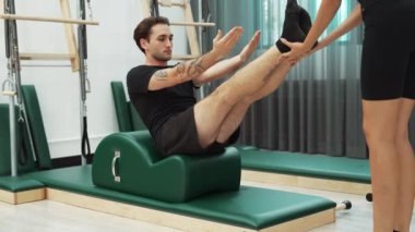Erkek müşteri pilates ark fıçısında bacak kaldırma alıştırması yapıyor. Vücut dengesini, bacak dayanıklılığını ve spor salonundaki esnekliğini arttırmak için eğitmen yardımı ile birlikte. Öğrenci yalancı ve muziplik pozu veriyor. Alışkanlık.