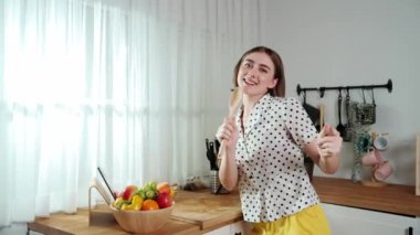 Enerjik beyaz anne kahvaltı için salata pişirirken ve yemek pişirirken elinde kepçeyle şarkı söylüyor. Sağlıklı yemek yapmaya hazırlanırken müziğe yönelen mutlu ev sahibi. Pedagoji.