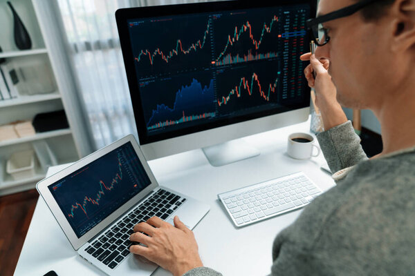 Business trader using computer and laptop to search highest profit value of dynamic increased stock market graph on working desk, analyzing exchange rate value on screen at modern office. Pecuniary.