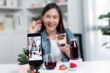 Seçici odaklı akıllı telefon ve gülümseyen genç, güzel Asyalı karışık çilek ve kiraz suyu detoksu değerlendirmesi sosyal medyada sağlıklı ürün tanıtımı sunuyor. Taktik.