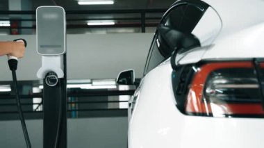 Yavaş çekim kadın, EV elektrikli arabasıyla şehir merkezindeki alışveriş merkezinin otoparkına gidiyor. Sürdürülebilirlik yaşam tarzını yeşil, temiz, yeniden şarj edilebilir elektrikli araç iç organlarıyla şarj ediyor.