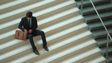 Akıllı bir iş adamının iş planı yapmak için telefon ve dizüstü bilgisayar kullanması. Merdivenlerde otururken. Müdür terfi alıyor, bilgisayarla arkadaşlarını ararken satışları arttırıyor. Sevinçli..