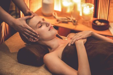 Beyaz kadın stres önleyici kafa masajı yapmaktan ve lüks otel veya otelde sıcak mum ışığında yüz güzelliği eğlencesi yapmaktan zevk alıyor. Sessiz.