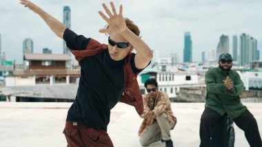 Bir grup profesyonel hip hop dansçısı çatıda break dans yapıyor. Becerikli koreograf serbest stil hareketini gösterirken, arkadaş da cesaretlendirir, alkışlar, alkışlar. Açık hava sporu 2024. Hiphop.