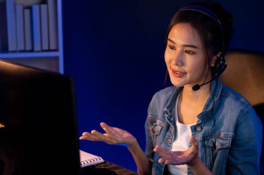 Sunucu kanalı Asyalı etkileyicisi canlı yayında konuşuyor. Sosyal medyada kulaklık takıyor, bilgisayar kaydı yapıyor, dinleyicileri selamlıyor ve Neon Modern Stüdyoları 'nda online olarak koçluk yapıyor. Taktik.