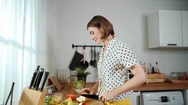 Enerjik anne, mutfak malzemeleri ile çevrili sebzeleri doğrarken modern mutfakta kahvaltı için salata yapıyor. Akıllı kadın temizlikçi yemek pişirir ve yemek hazırlar. Sağlıklı bir yaşam tarzı. Pedagoji.