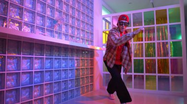 Komik break dansçı kameraya bakarken hiphop 'a doğru serbest adım atıyor. Çılgın mutlu hipster dans edip sokak dansı yaparken Led ışığında günlük kıyafet ve güneş gözlüğü takıyor. Mutluluk.