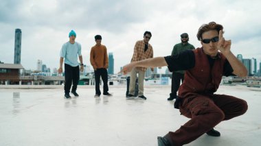 Profesyonel Asyalı sokak dansçısı çatıda çok kültürlü arkadaşlar dans ederken B boy dansı yapıyor. Genç modern dans grubu hip hop hareketi yapıyor. Tarz, moda, aksiyon. Açık hava sporu 2024. Hiphop.